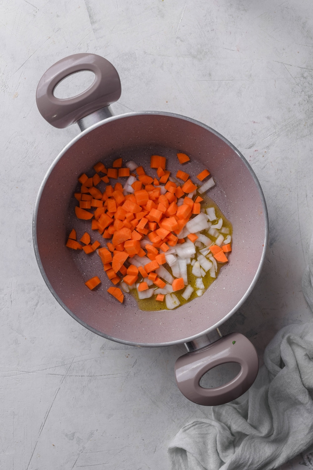 A pot filled with diced carrots, onion, and oil.