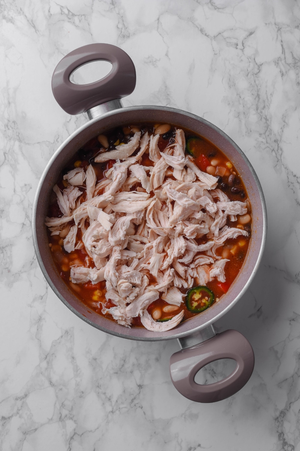 A pot filled with shredded chicken, corn, jalapeños, beans, and broth.