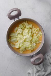 A pot filled with soup and a pile of cabbage on top.