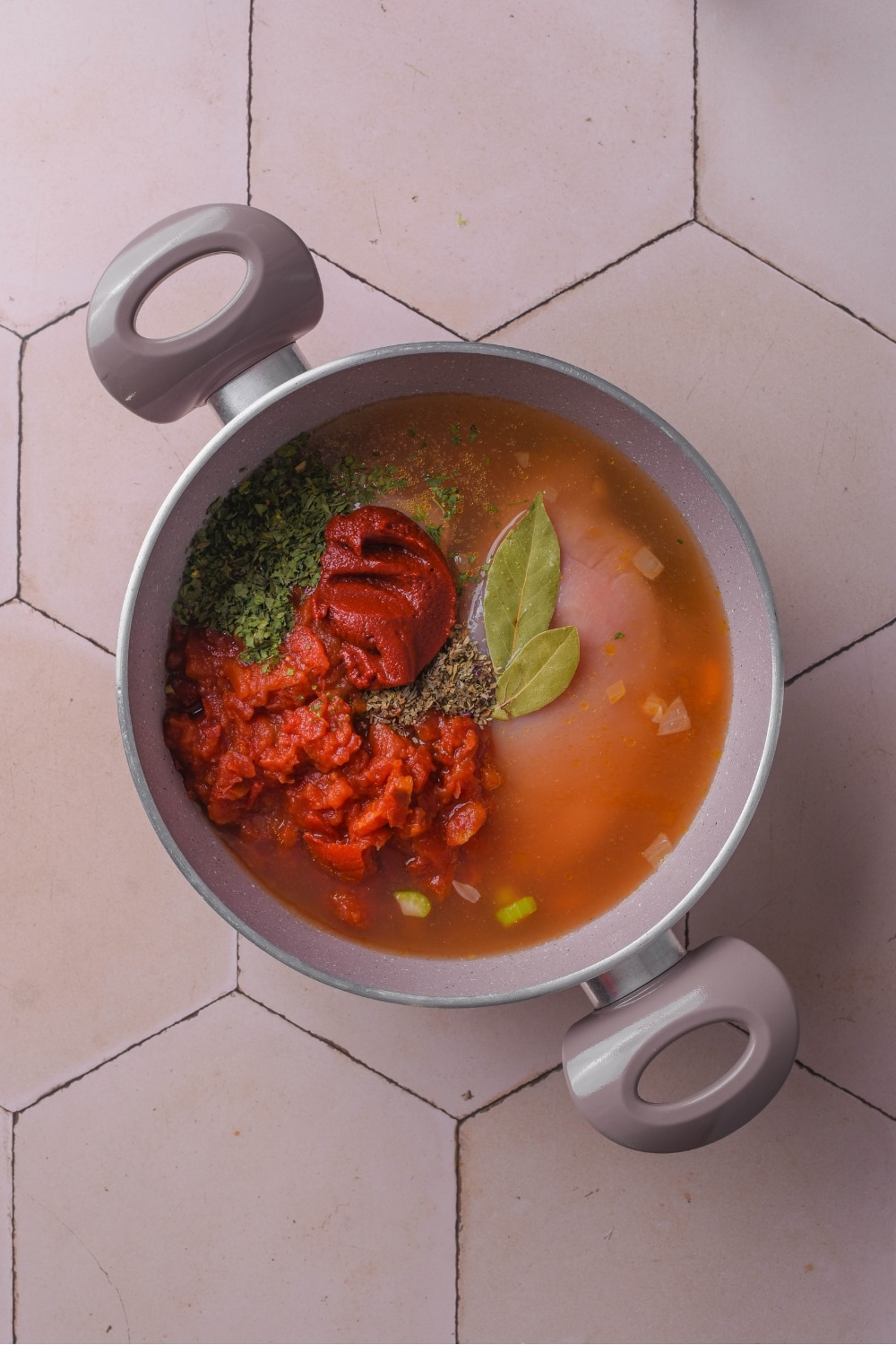 A pot filled with crushed tomatoes, tomato paste, seasonings, and raw chicken covered in broth.