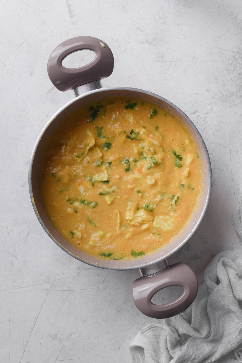 A pot filled with creamy soup with kale and cabbage floating in the soup.