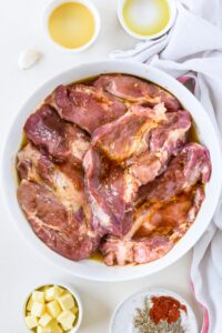 A bowl filled with raw marinating pork chops.