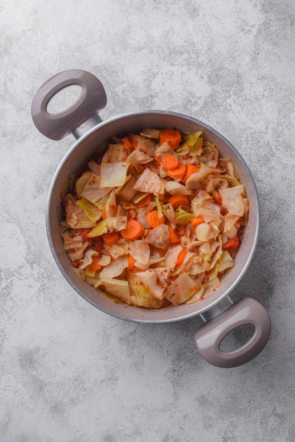 A pot filled with cabbage soup in a red broth with chunks of sliced carrots mixed in.