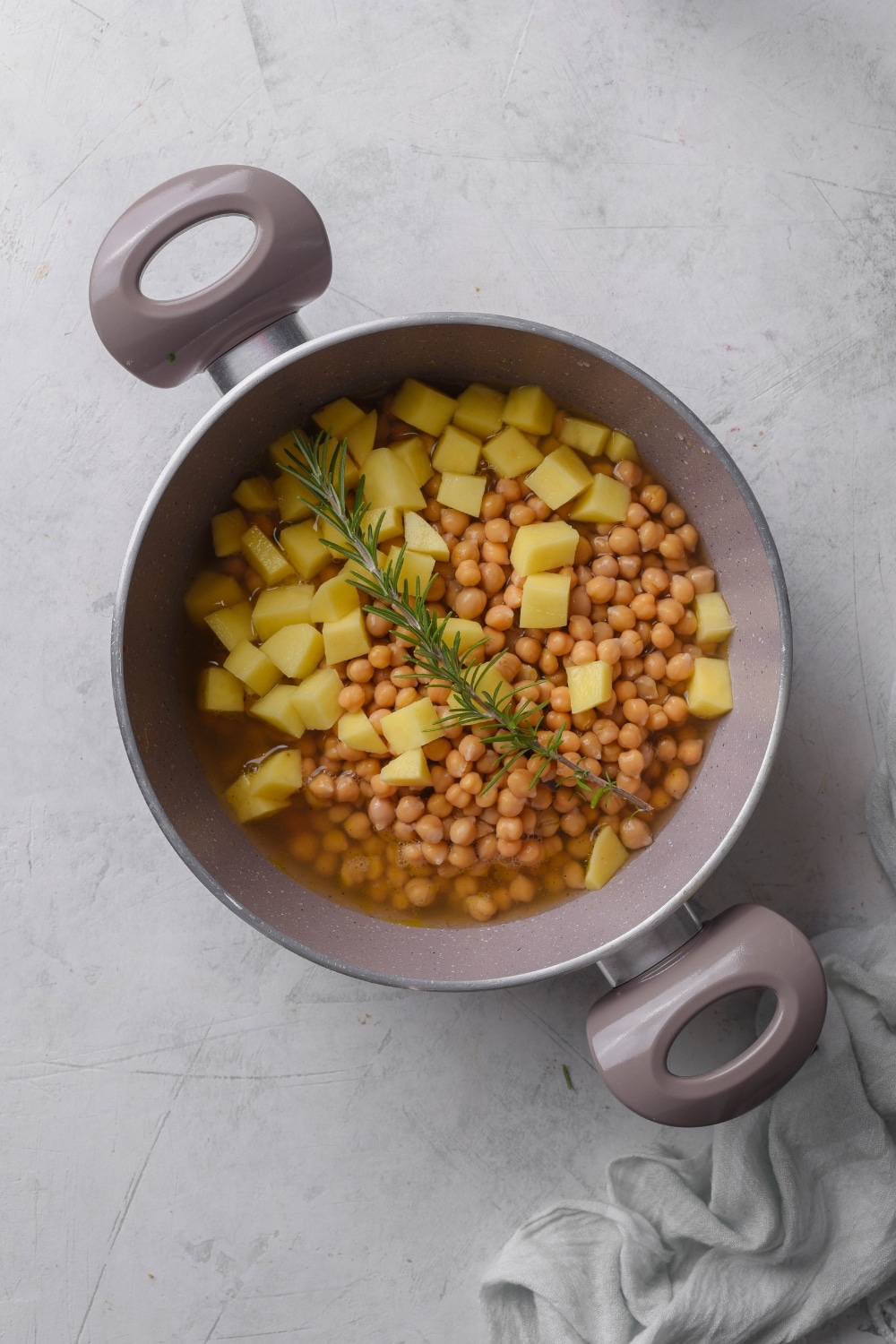 A pot filled with chickpeas, cubed potatoes, rosemary, and broth.