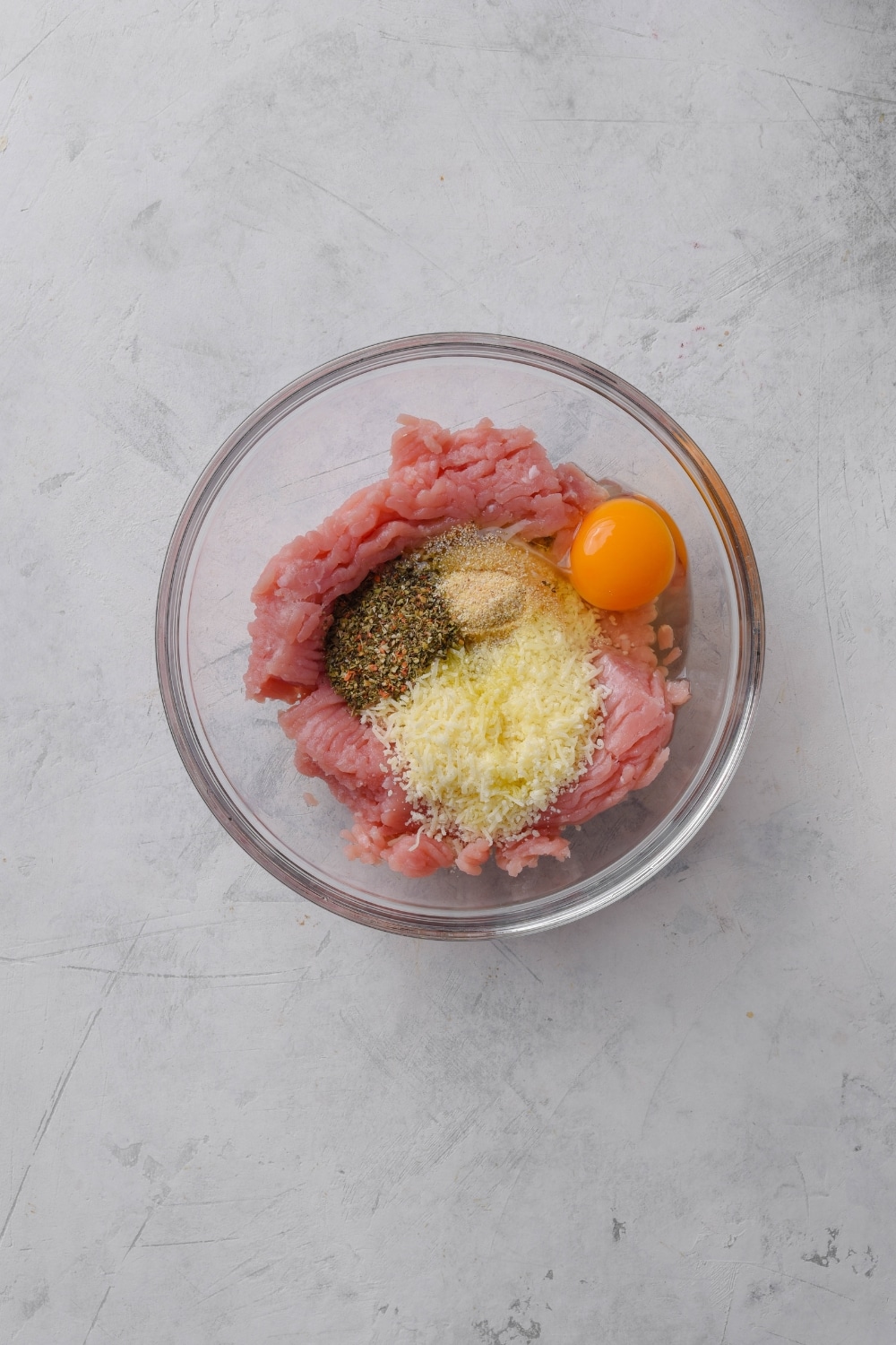 A bowl filled with raw ground turkey, an egg, parmesan cheese, and seasonings.