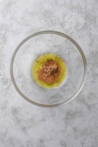 A clear bowl filled with mustard, oil, vinegar, and spices.