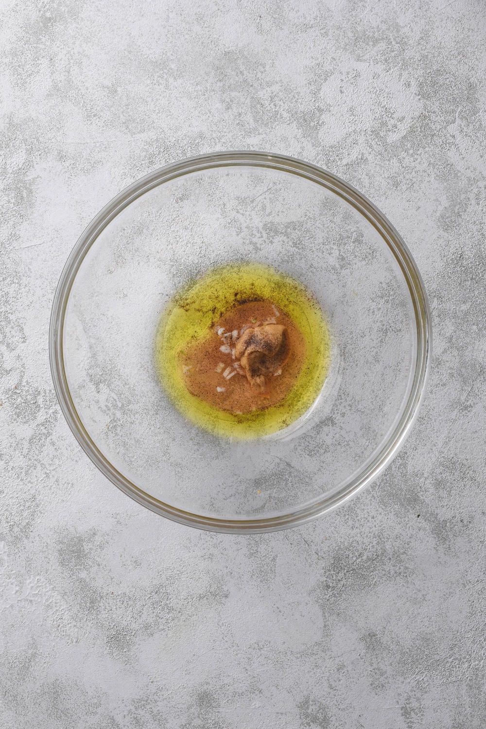 A clear bowl filled with mustard, oil, vinegar, and spices.