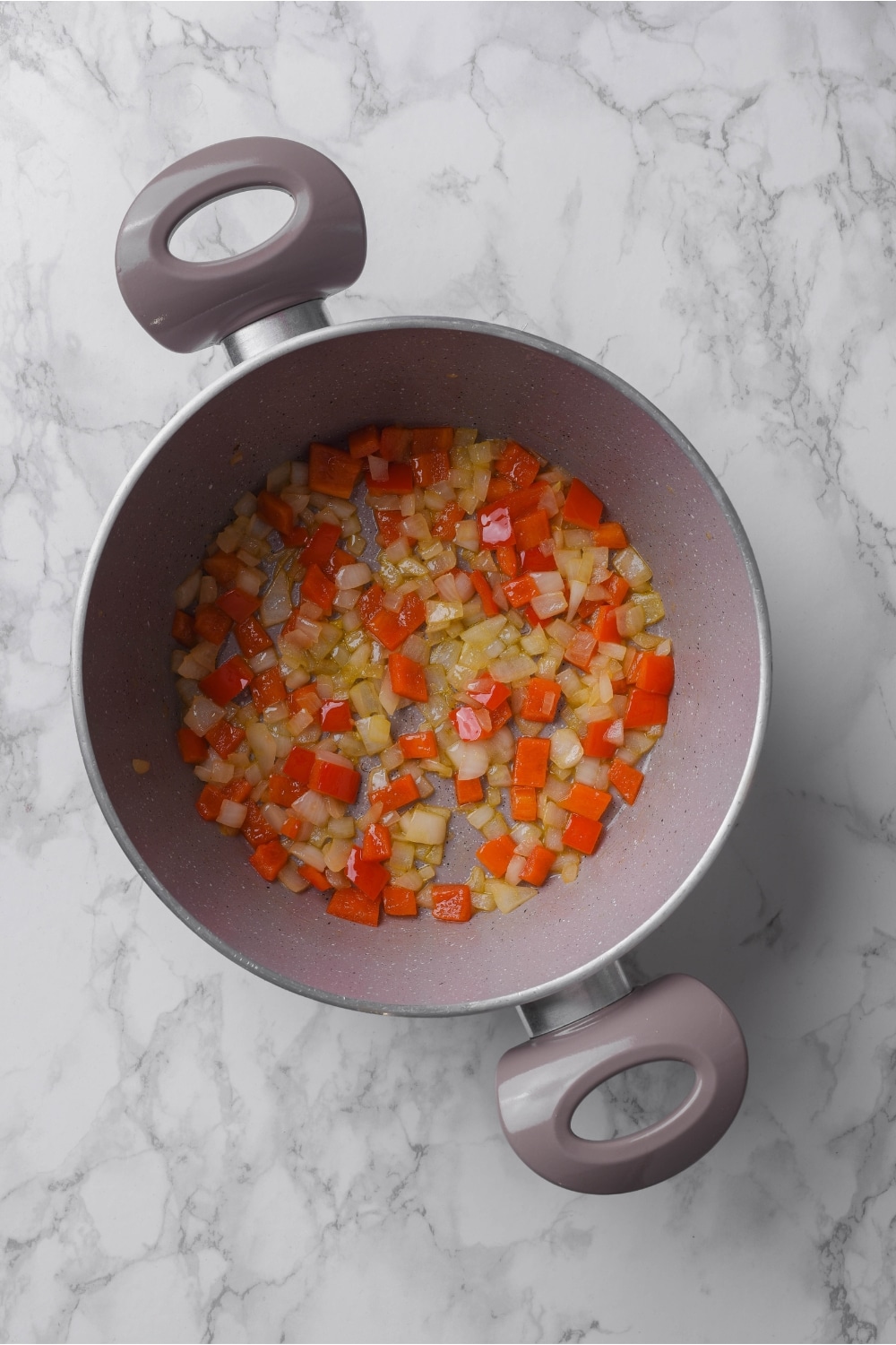 A pot filled with diced peppers and onions cooking in it.