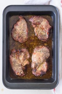 A baking dish filled with cooked pork chops in a brown marinade.