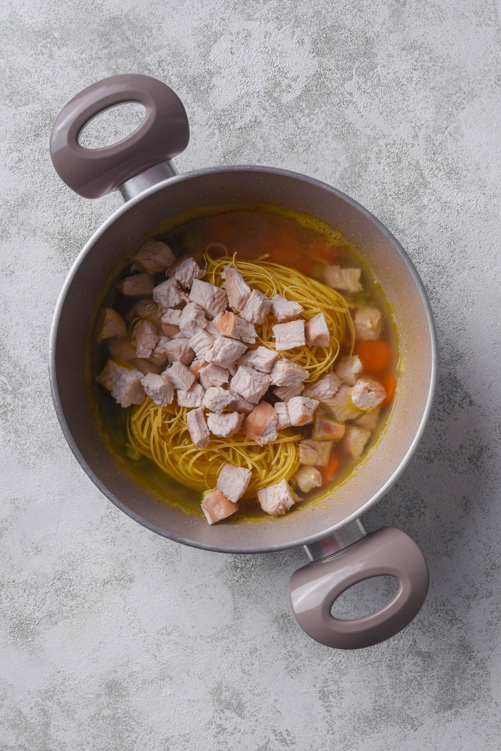 A pot filled with stock, pasta, diced turkey, and carrots.