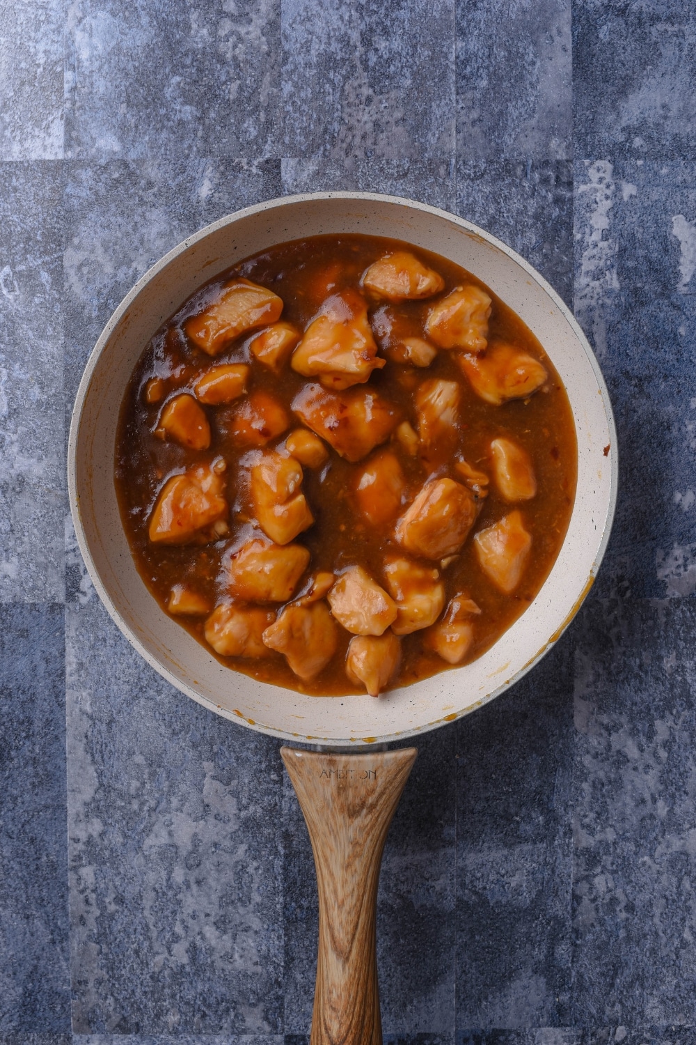 A skillet filled with chicken pieces in a thick orange sauce.