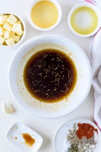 A bowl filled with a marinade. The bowl is surrounded by empty bowls of ingredients and a bowl of butter cubes.