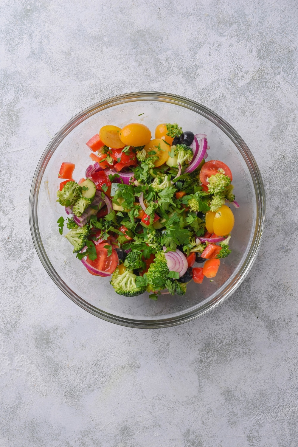 A clear bowl filled with broccoli, cherry tomatoes, red onion, peppers, and fresh herbs.