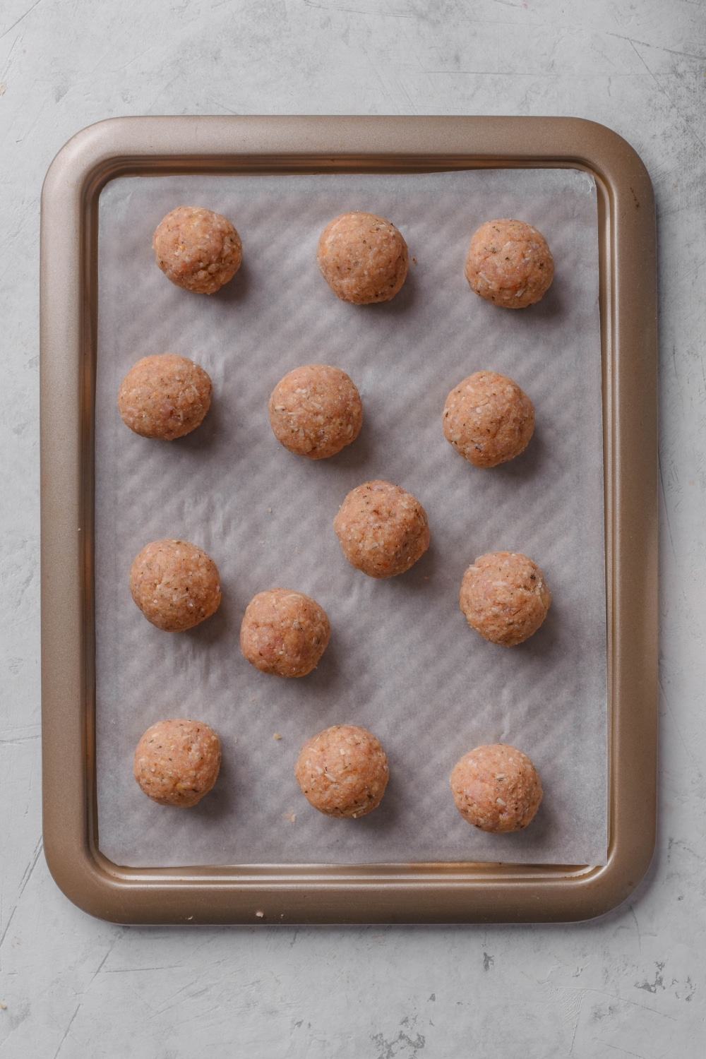 Thirteen unbaked meatballs evenly spaced on a baking sheet lined with parchment paper.