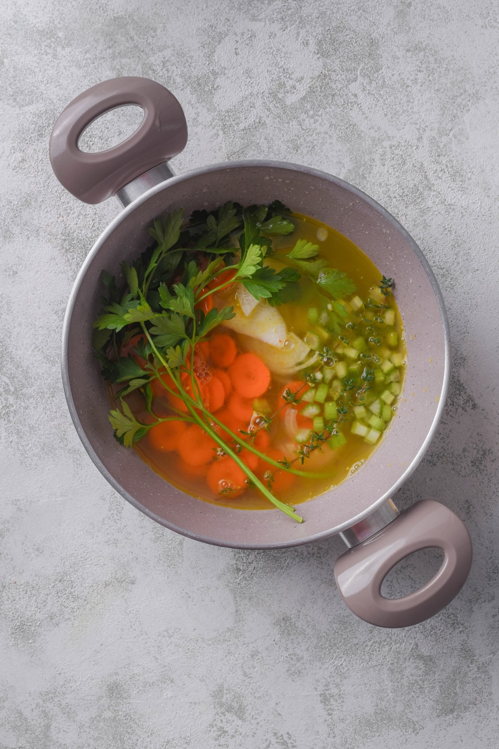 A pot filled with broth, celery, carrots, onion, and fresh herbs.