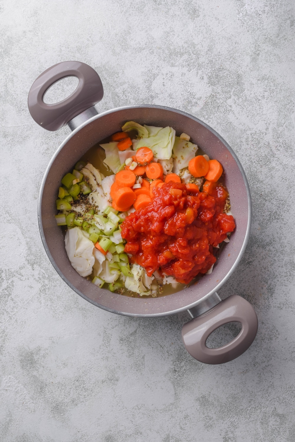 A pot filled with carrots, celery, cabbage, crushed tomatoes, broth, and seasonings.