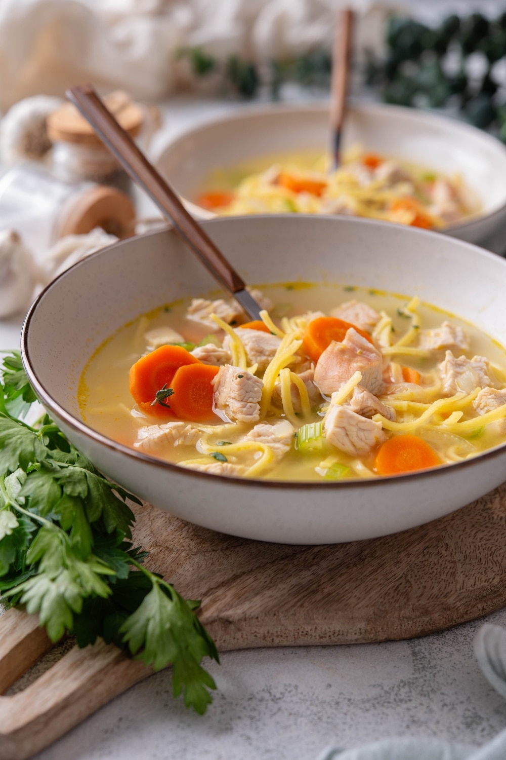 A bowl of turkey noodle soup with chunks of carrots and celery. There is a spoon in the bowl and a second bowl in the background.