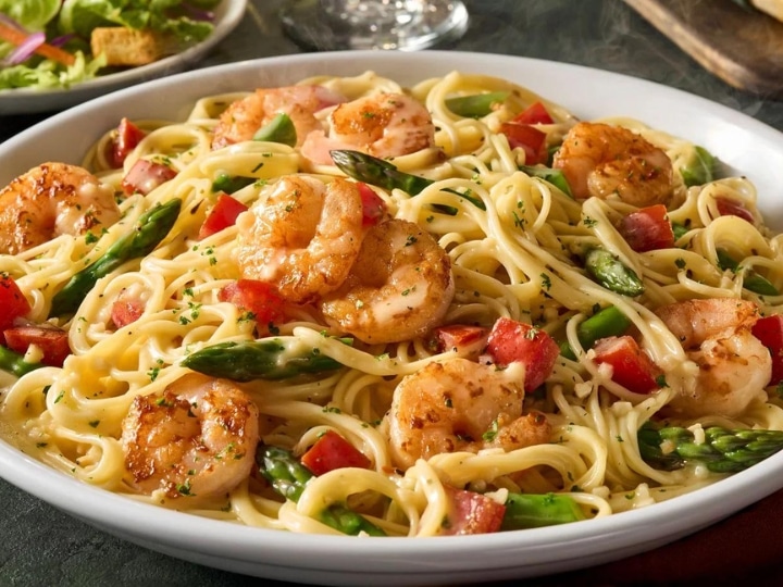 Shrimp, asparagus, and tomatoes with spaghetti and sauce in a bowl.