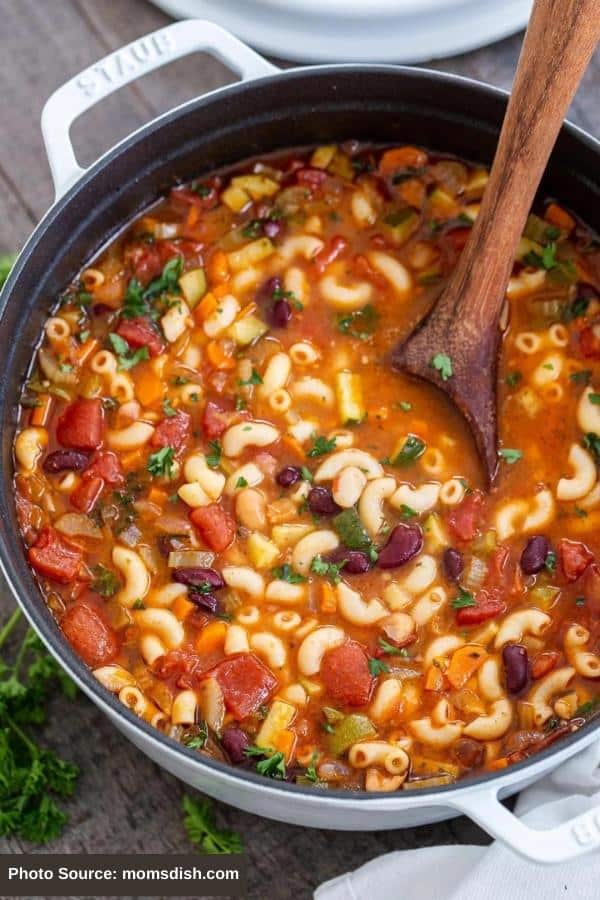 A pot filled with elbow noodles, beans, tomatoes, herbs, and broth.