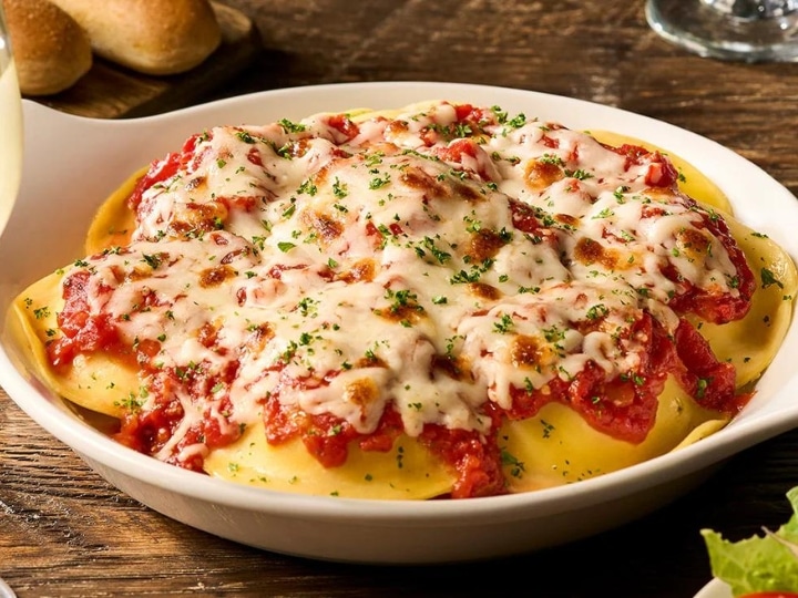 Melted cheese on top of marinara sauce on cheese ravioli in a white bowl.