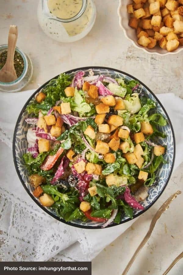 A bunch of croutons on top of mixed greens and red onion in a large bowl on top of a tablecloth.