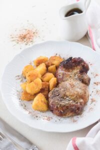 A seasoned pork chop on a plate with tater tots.