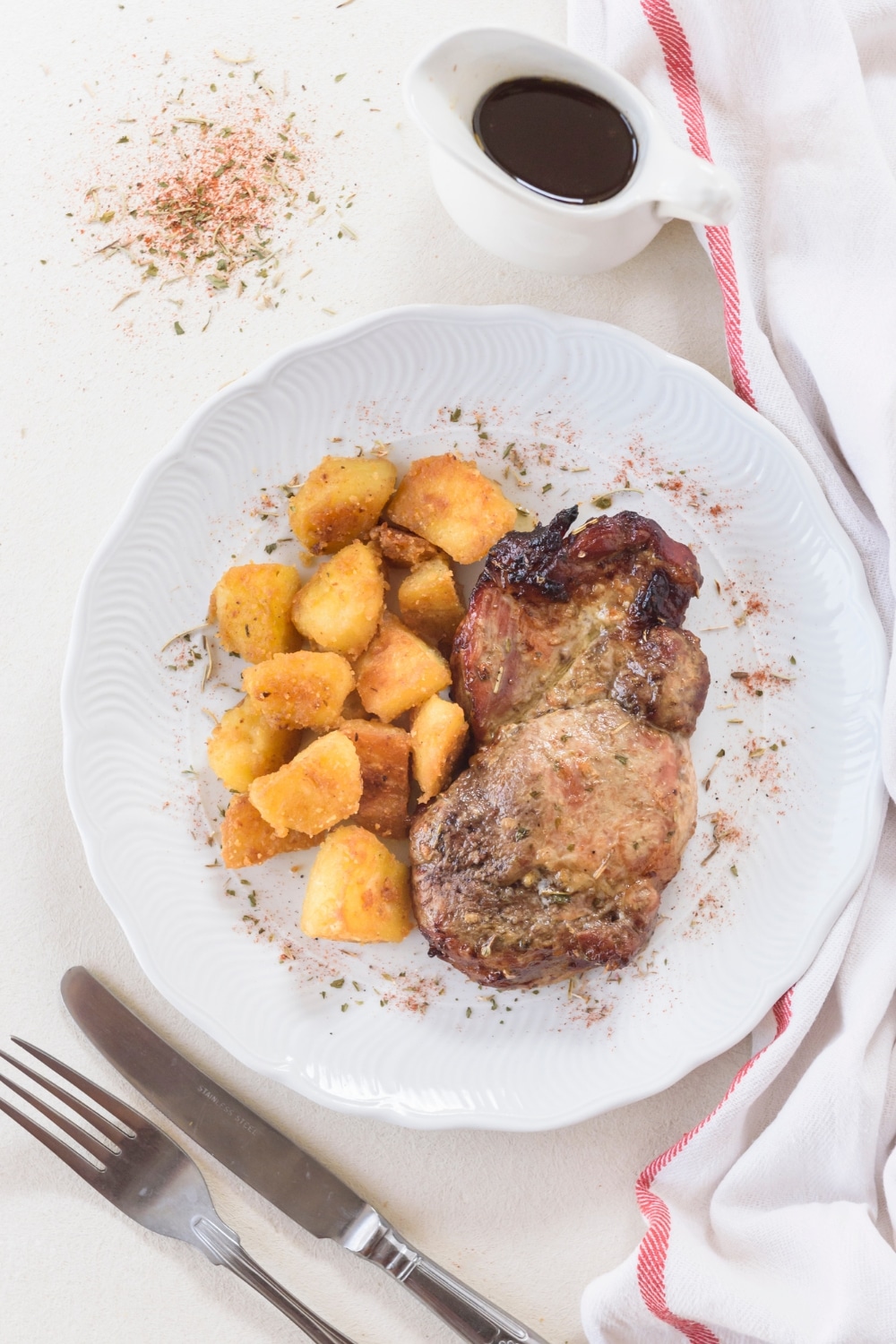 A seasoned pork chop on a plate with tater tots and a pitcher of gravy next to the plate.