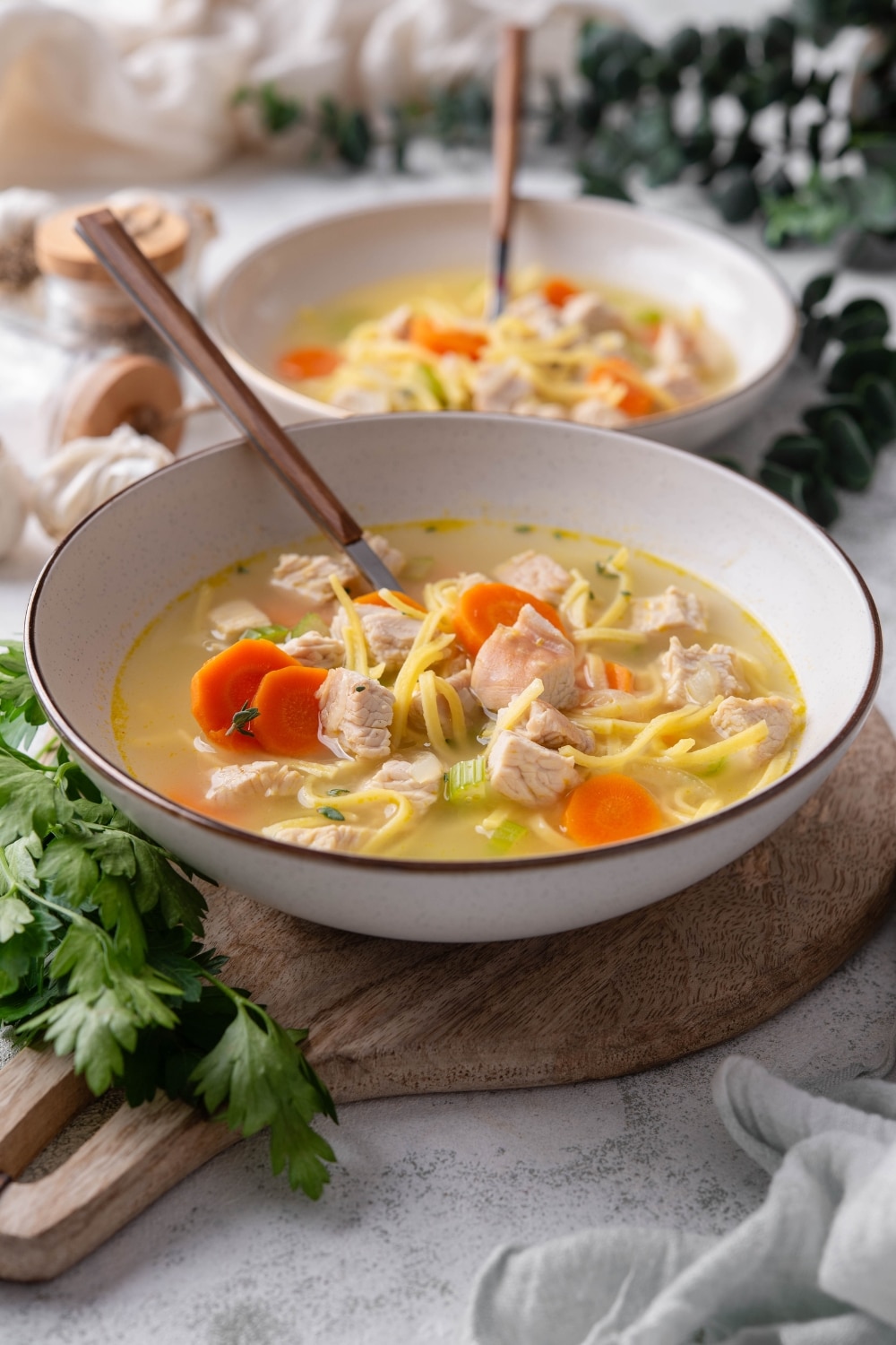 A bowl of turkey noodle soup with chunks of carrots and celery. There is a spoon in the bowl and a second bowl in the background.