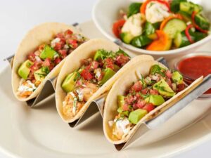 Three cheesecake facotry Skinnylicious Chicken Soft Tacos in a metal taco holder on a plate.