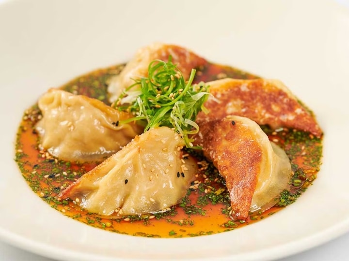 Five cheesecake factory Chicken Pot Stickers in a sauce in a white bowl.