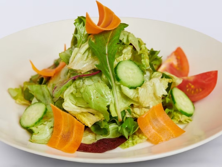 Mixed greens and sliced cucumber on a white plate.