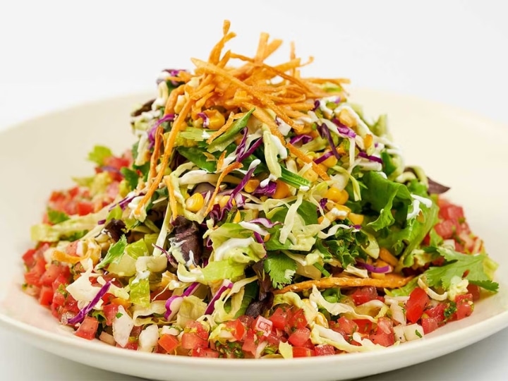 Crispty fried onions on top of salad mix with diced tomatoes on a plate.