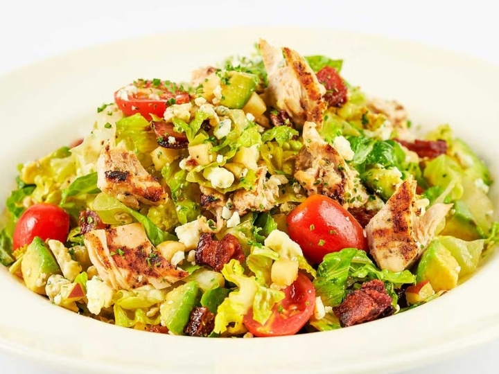 Grilled chicken and chopped salad greens with tomatoes in a white bowl .