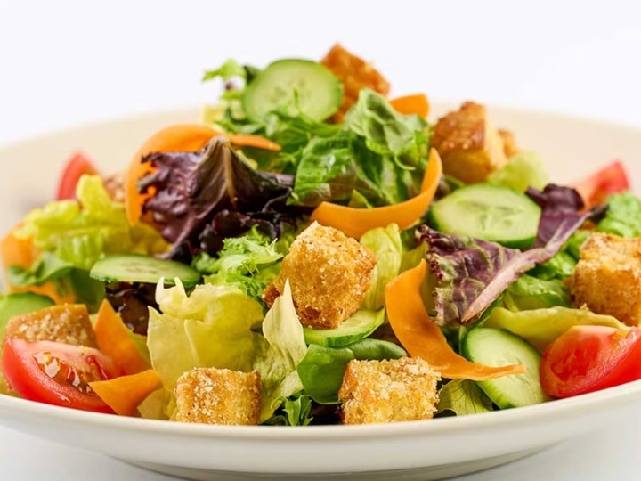 Mixed salad greens, croutons, sliced cucumber, and tomatoes on a white plate.