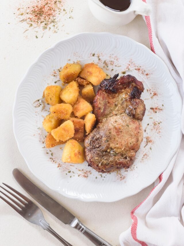 A seasoned pork chop on a plate with tater tots and a pitcher of gravy next to the plate.