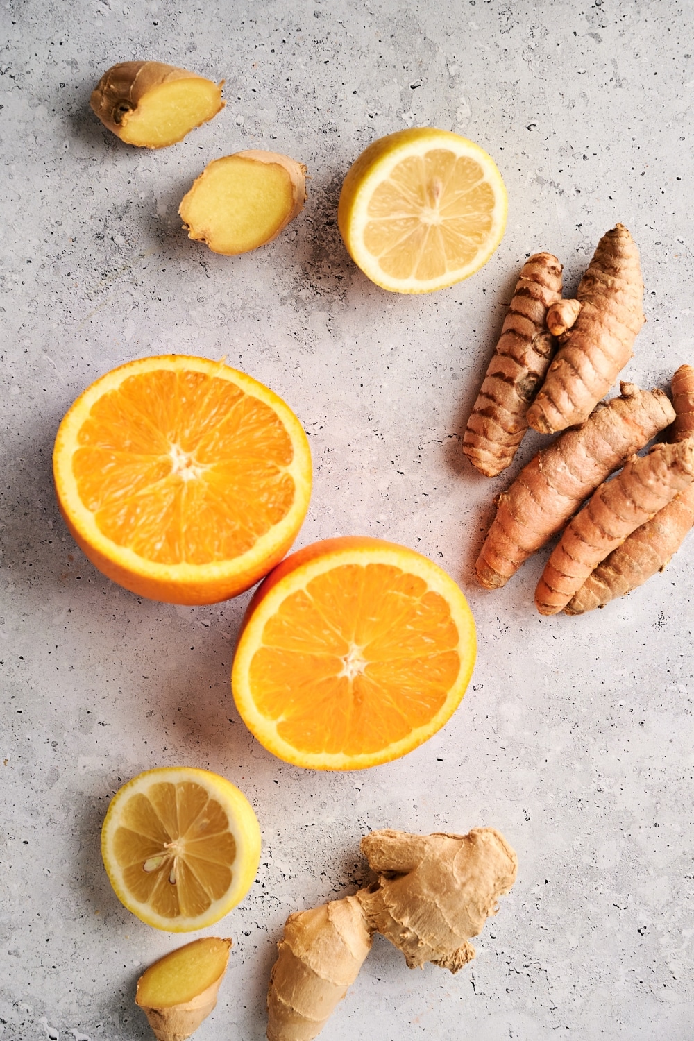 A countertop with an orange, lemon, ginger, and turmeric on it.