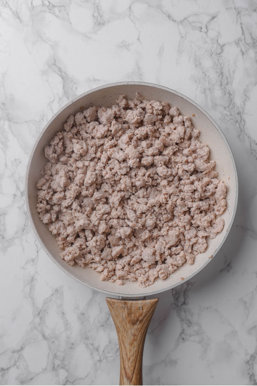 Cooked ground turkey in a white ceramic pan with a wooden handle on top a marble countertop.