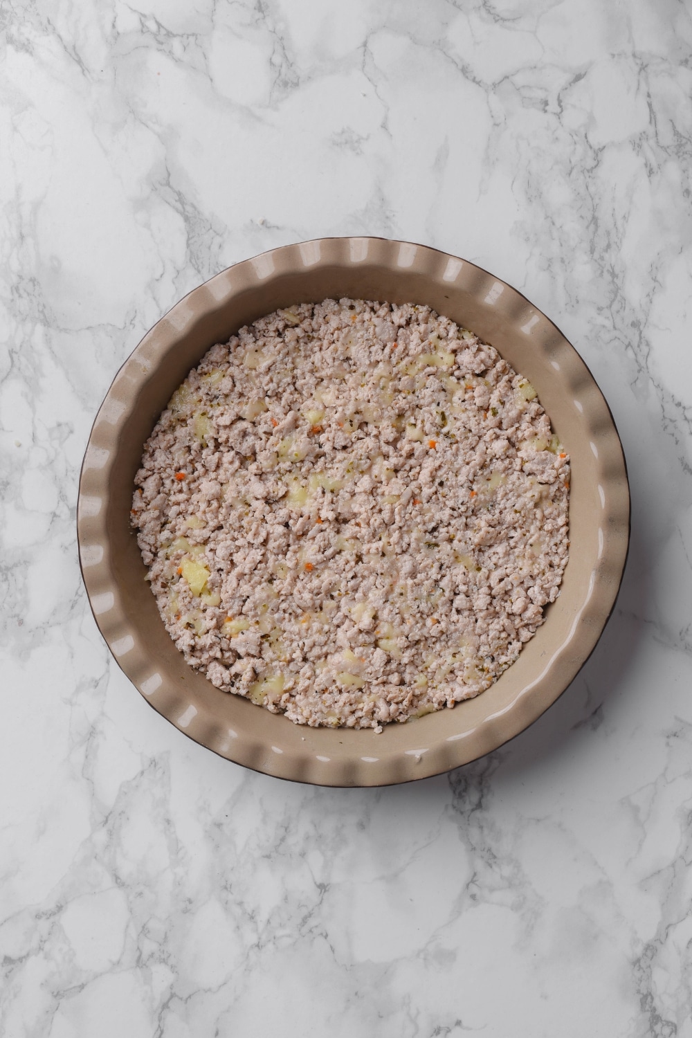 A pie pan filled with cooked ground turkey on a white marble countertop.