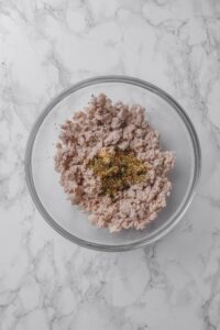 Cooked ground turkey and seasoning in a glass bowl on a marble countertop.