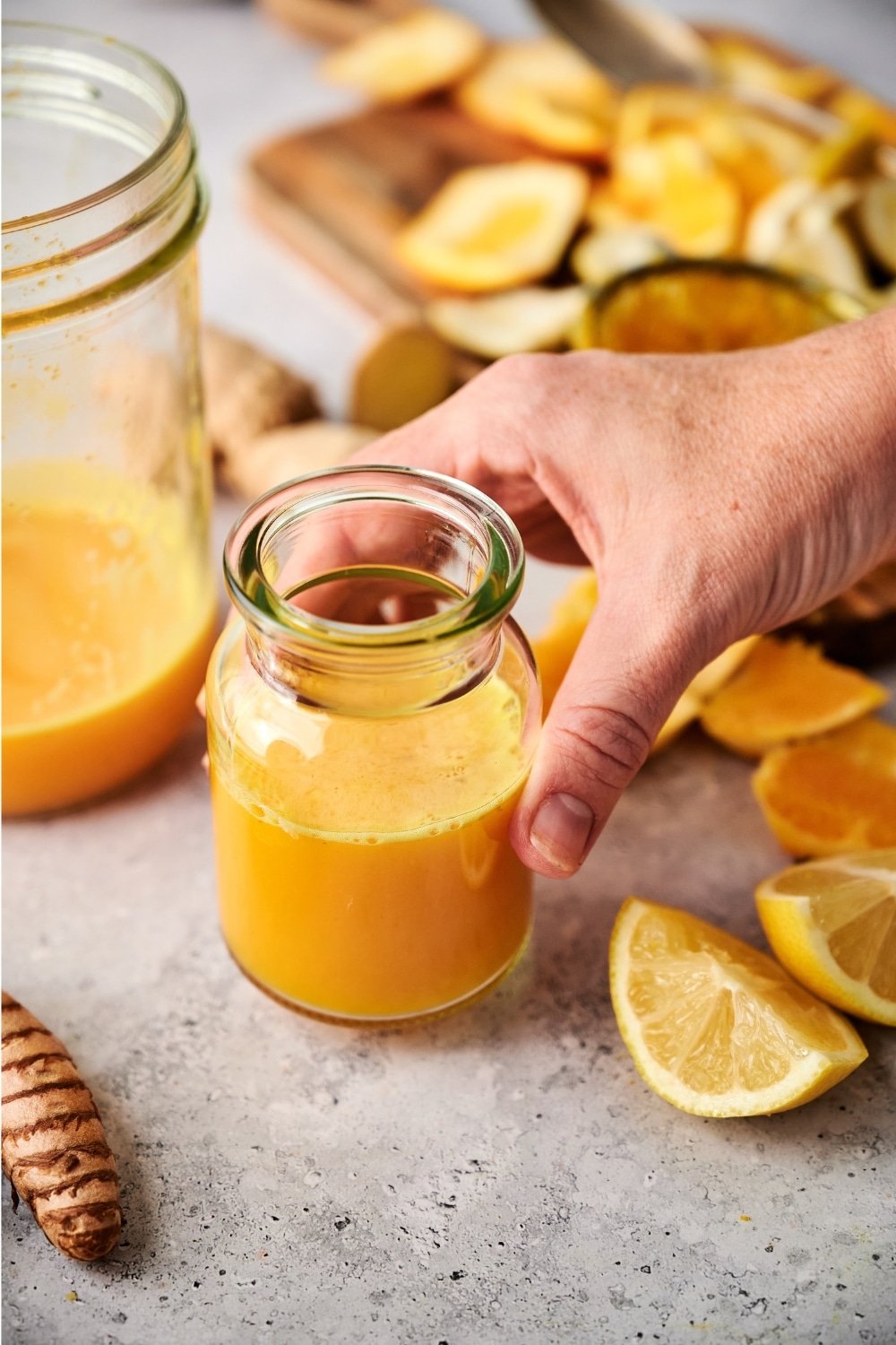 A hand holding a small glass with a ginger turmeric shot in it.