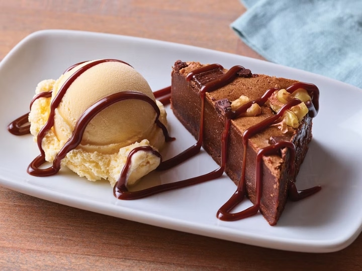 A slice of a brownie on a white plate with a scoop of vanilla ice cream next to it.