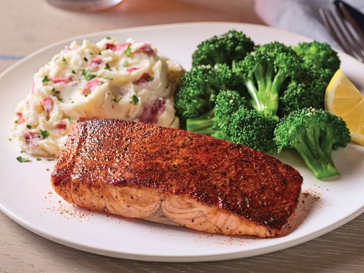 A filet of salmon on a white plate next to mashed potatoes and broccoli.