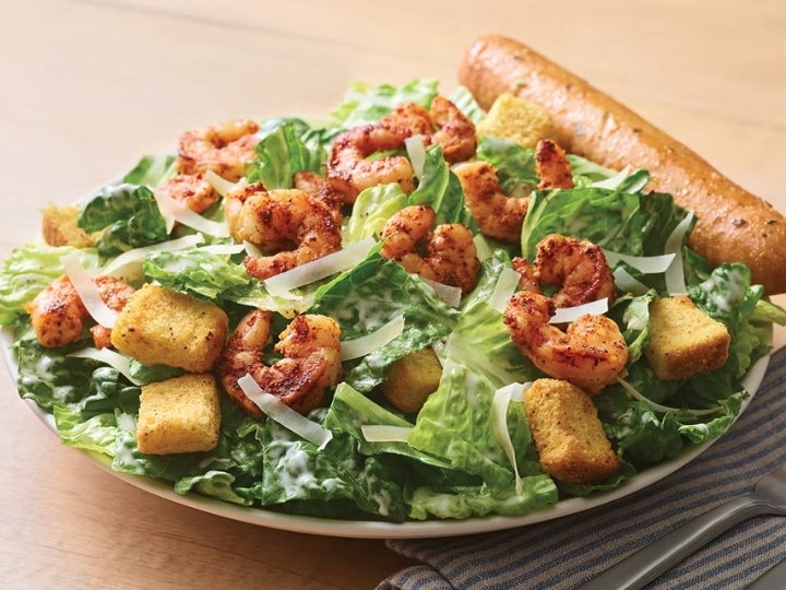 Blackened shrimp and croutons on top of a bed of greens.