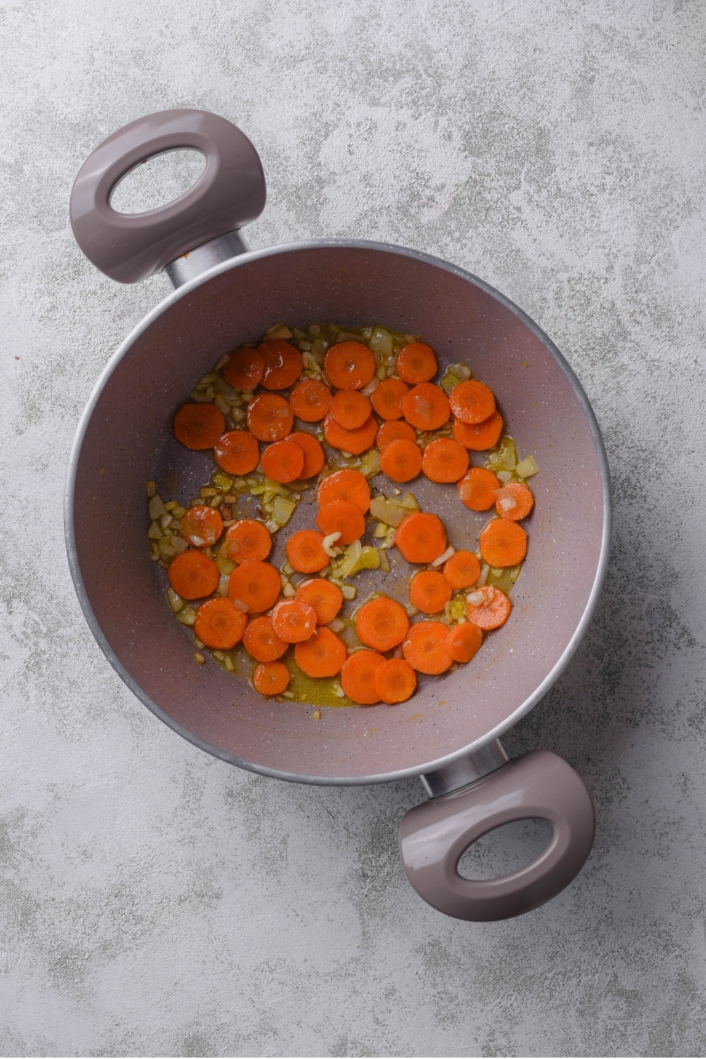 A large pot with sliced carrots, garlic, and onions cooking in olive oil.