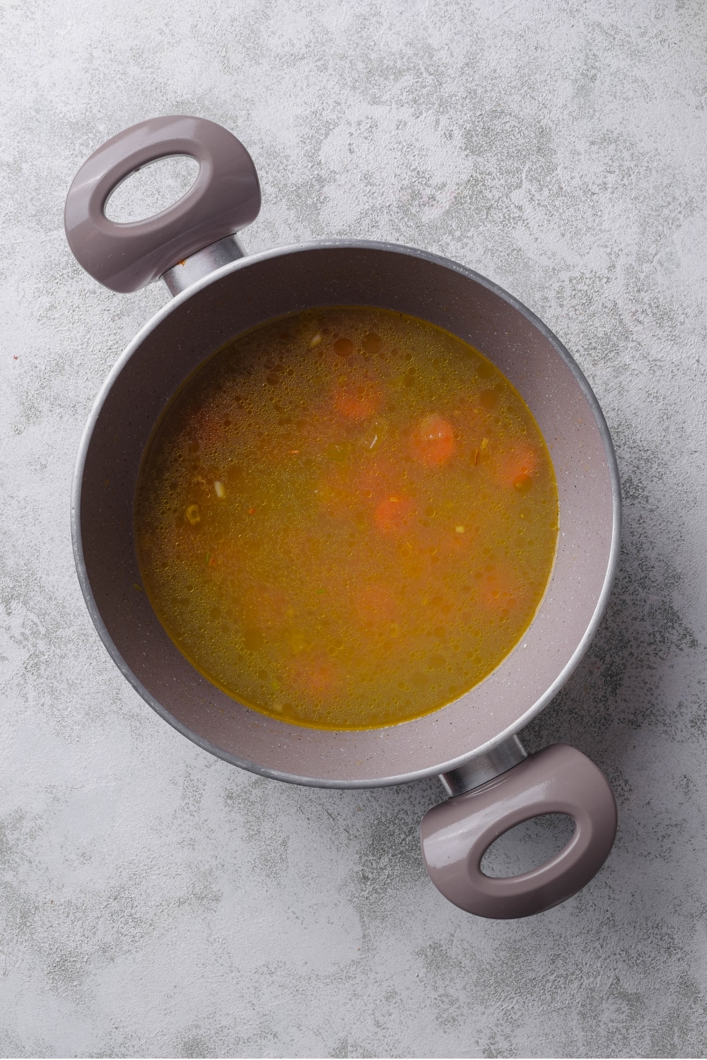 A large pot with carrots cooking in chicken broth.