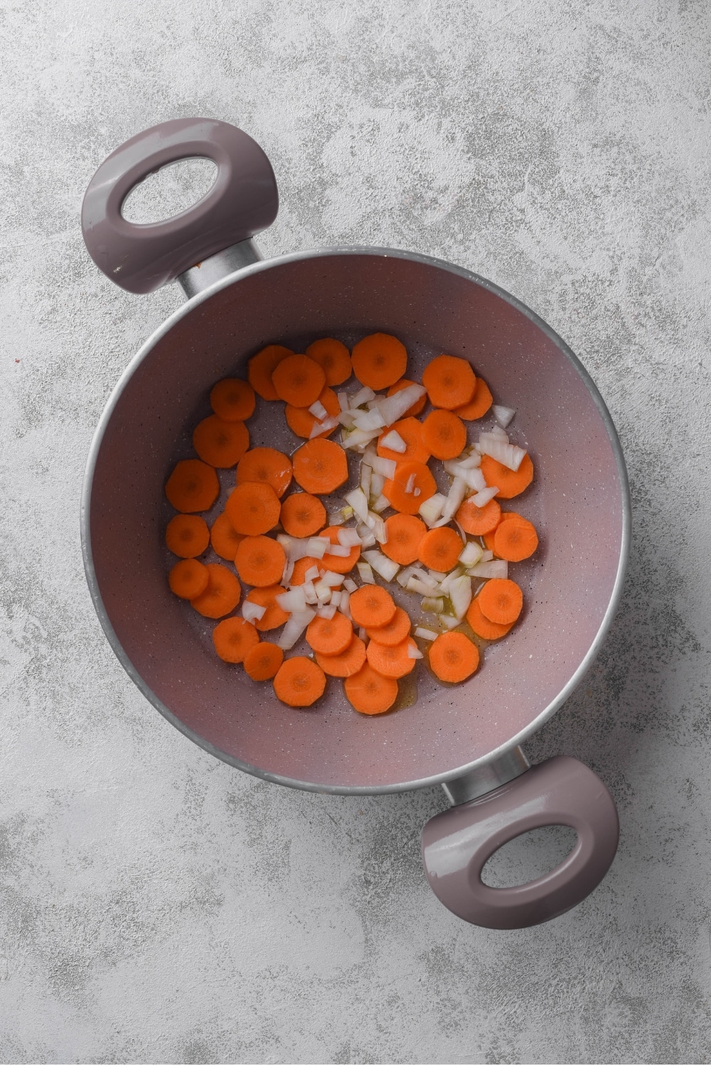 A large pot with sliced carrots and onions cooking in olive oil.