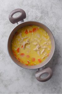 A large pot filled with creamy chicken broth, carrots, and shredded chicken.