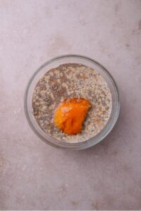 A glass bowl filled with oats, milk, chia seeds, and pumpkin on top.