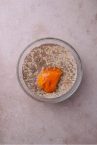A glass bowl filled with oats, milk, chia seeds, and pumpkin on top.