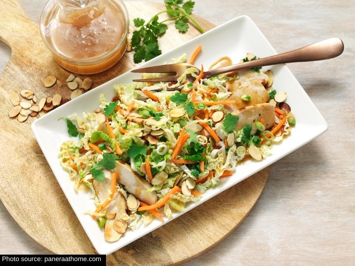 A cabbage and carrot mi with sliced chicken and almonds on a rectangular plate with a fork on it. Behind it is a jar of dressing.